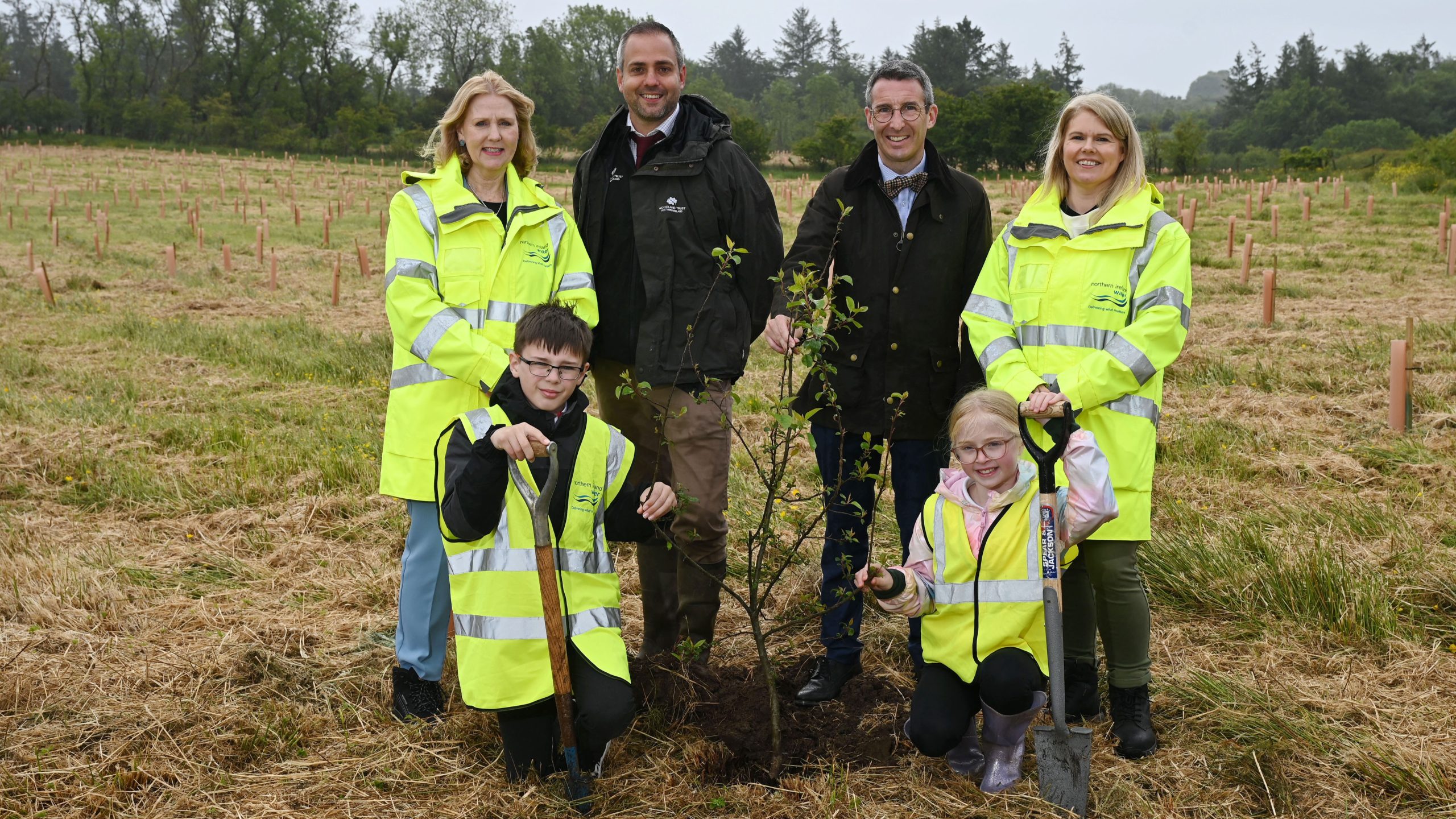 (Back row) Jo Aston, Chair at NI Water; Matt Huddlestone, Senior Outreach Manager for the Woodland Trust Northern Ireland; DAERA Minister, Andrew Muir and Dr Sara Venning, CEO NI Water.(Front row) Local schoolchildren from Woodburn and Oakfield Primary Schools. 